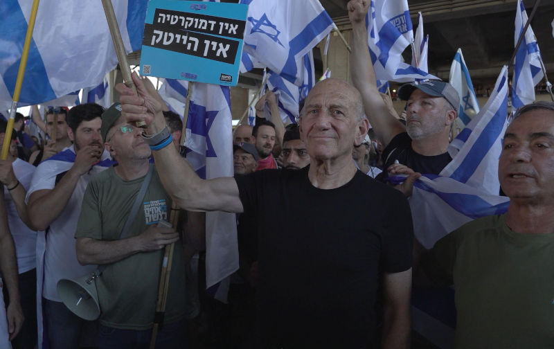 Former prime minister Ehud Olmert holds the Israeli flag during a demonstration held by anti government protestors outside Israel’s main international airport against PM Benjamin Netanyahu and Israel’s hard-right government judicial system plan that aims to weaken the country’s Supreme Court, at Ben Gurion Airport near Tel Aviv on July 3, 2023 in Lod, Israel Image: Alamy / Eddie Gerald Former prime minister Ehud Olmert holds the Israeli flag during a demonstration held by anti government protestors outside Israel's main international airport against PM Benjamin Netanyahu and Israel's hard-right government judicial system plan that aims to weaken the country's Supreme Court, at Ben Gurion Airport near Tel Aviv on July 3, 2023 in Lod, Israel Image: Alamy/Eddie Gerald