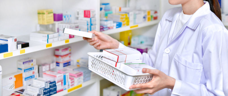 Pharmacist chemist woman standing refills the shelves with new stocks in pharmacy.