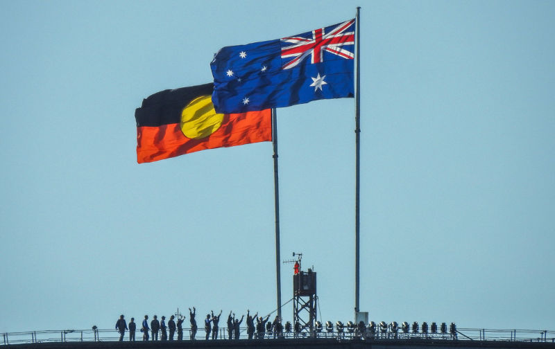 The Australian and Australian Aboriginal flags fly on the Sydney Harbour Bridge on a windy and sunny afternoon in summer.