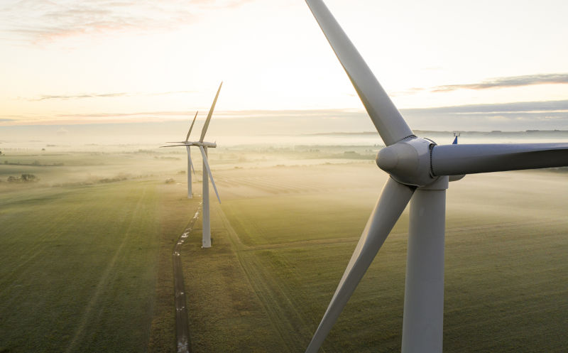 Aerial view of three wind turbines in the early morning fog at sunrise.