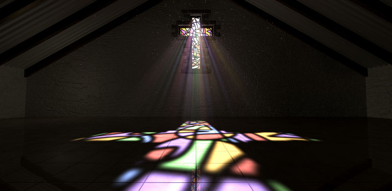 An interior building with a colourful stained glass window in the shape of a crucifix with a spotlight rays penetrating through it reflecting the image on the floor.