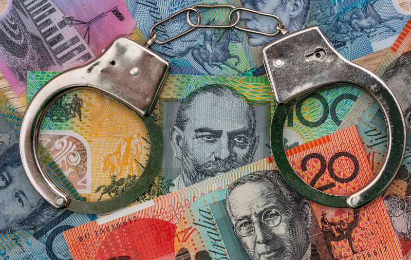 Australian dollar banknotes with handcuffs on wooden table.