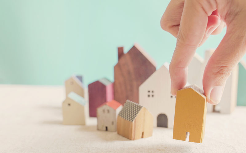 Hand choosing yellow miniature house, searching right property.