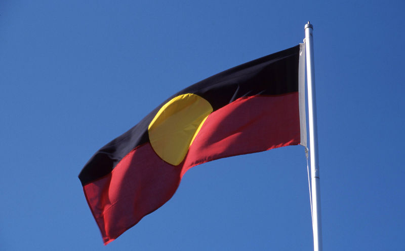 Australian Aboriginal flag blowing in a brisk breeze on a flagpole.