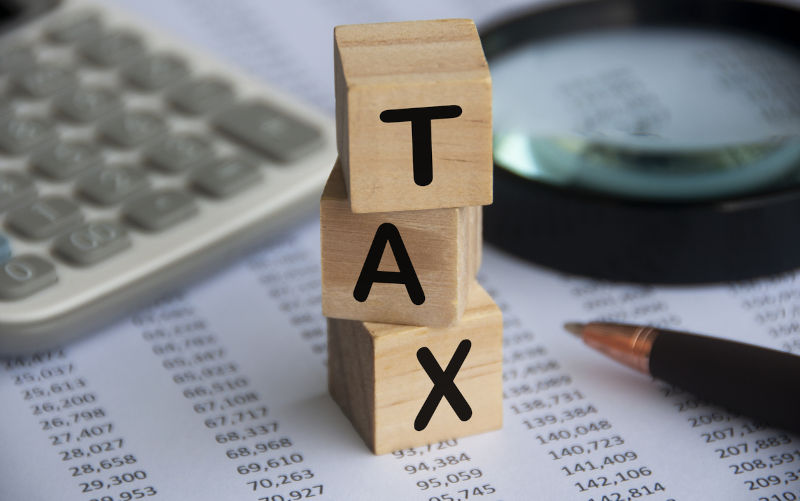 Tax word on wooden blocks with calculator, pen, magnifying glass and data analysis background. Tax concept