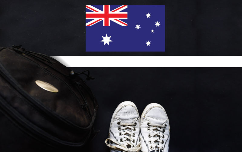 A man with a shoes and backpack is standing on asphalt next to flag of Australia and border