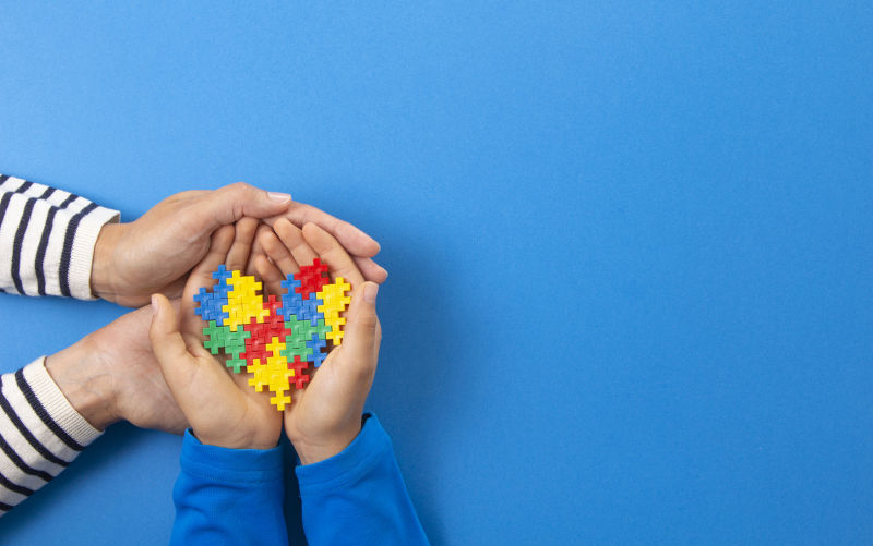 Adult and child hands holding puzzle heart on light blue background