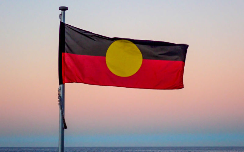 The Australian Aboriginal flag flies at Bondi Beach, Sydney at sunset in winter on 16 June 2023. In the background is the Pacific Ocean.