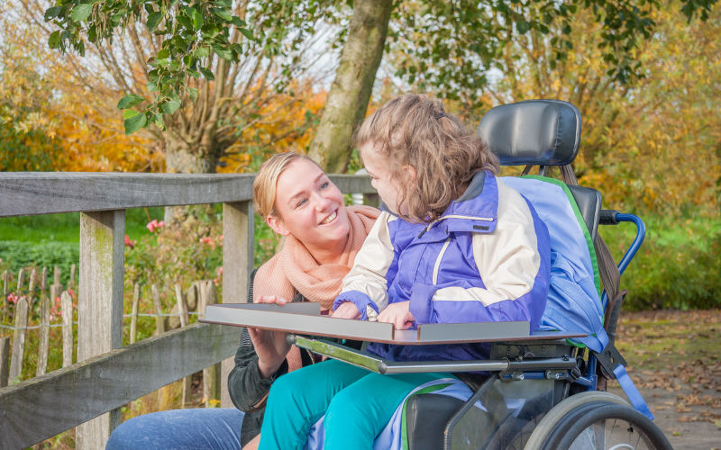 Working together with disability.A disabled child in a wheelchair being cared for by a voluntary care worker