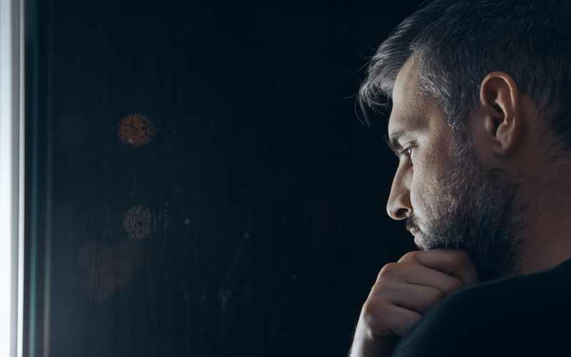 Man with beard holding his chin beside window at night