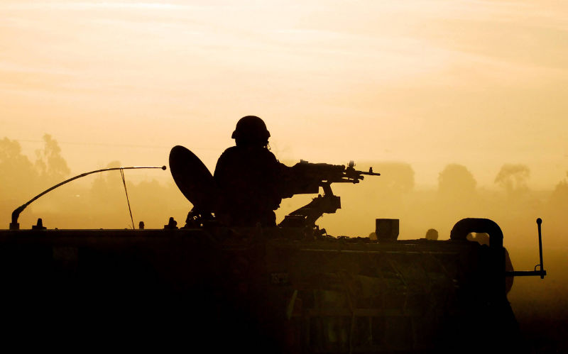 Silhouette of an army soldier preparing his tank and weapons at sunset