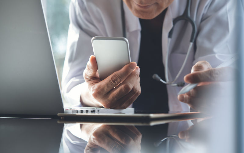 Close up, doctor using mobile smart phone, working on laptop computer during the conference with stethoscope on desk, digital data, medical electronic record system, medical technology background